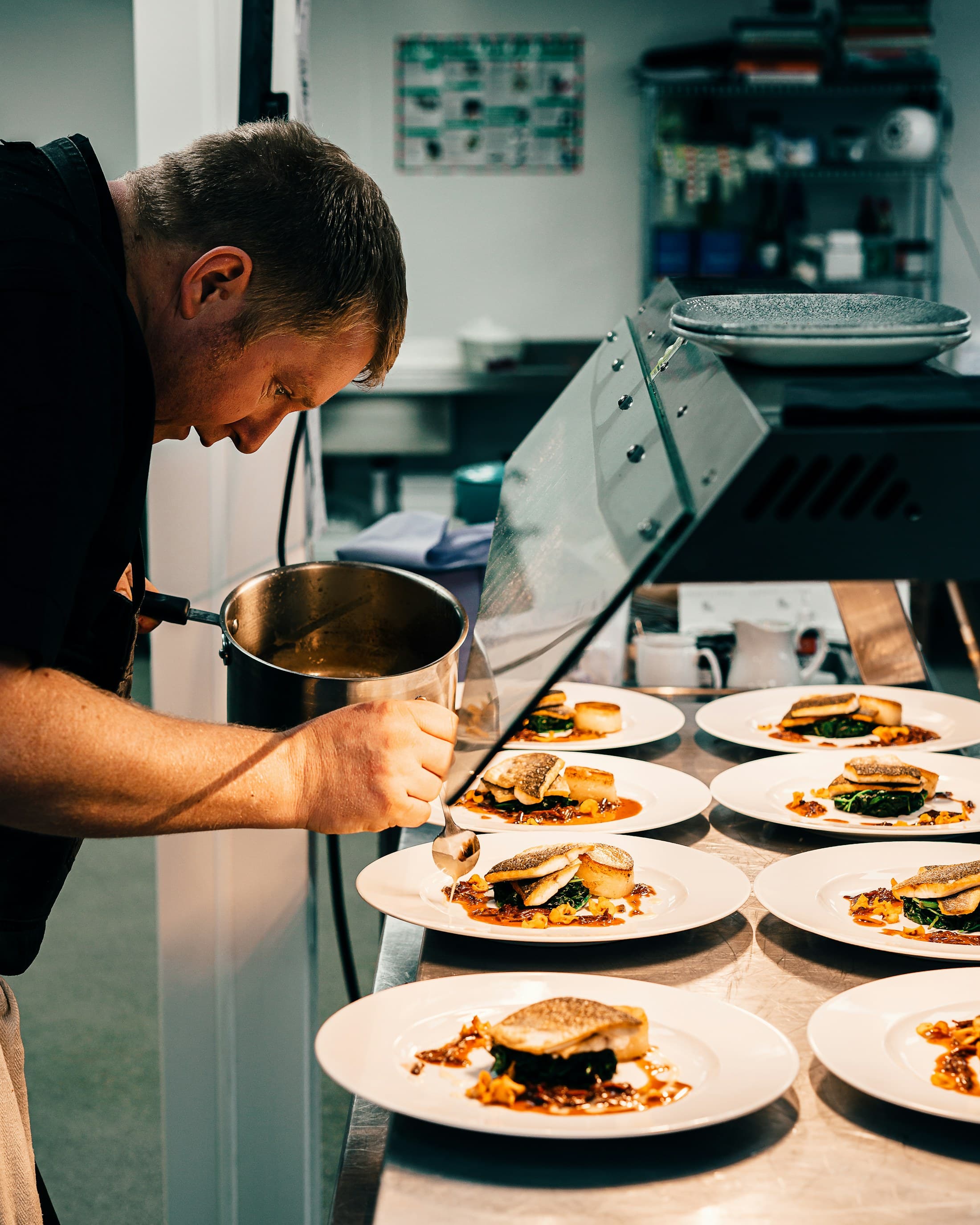 A chef saucing a row of plates at the pass.