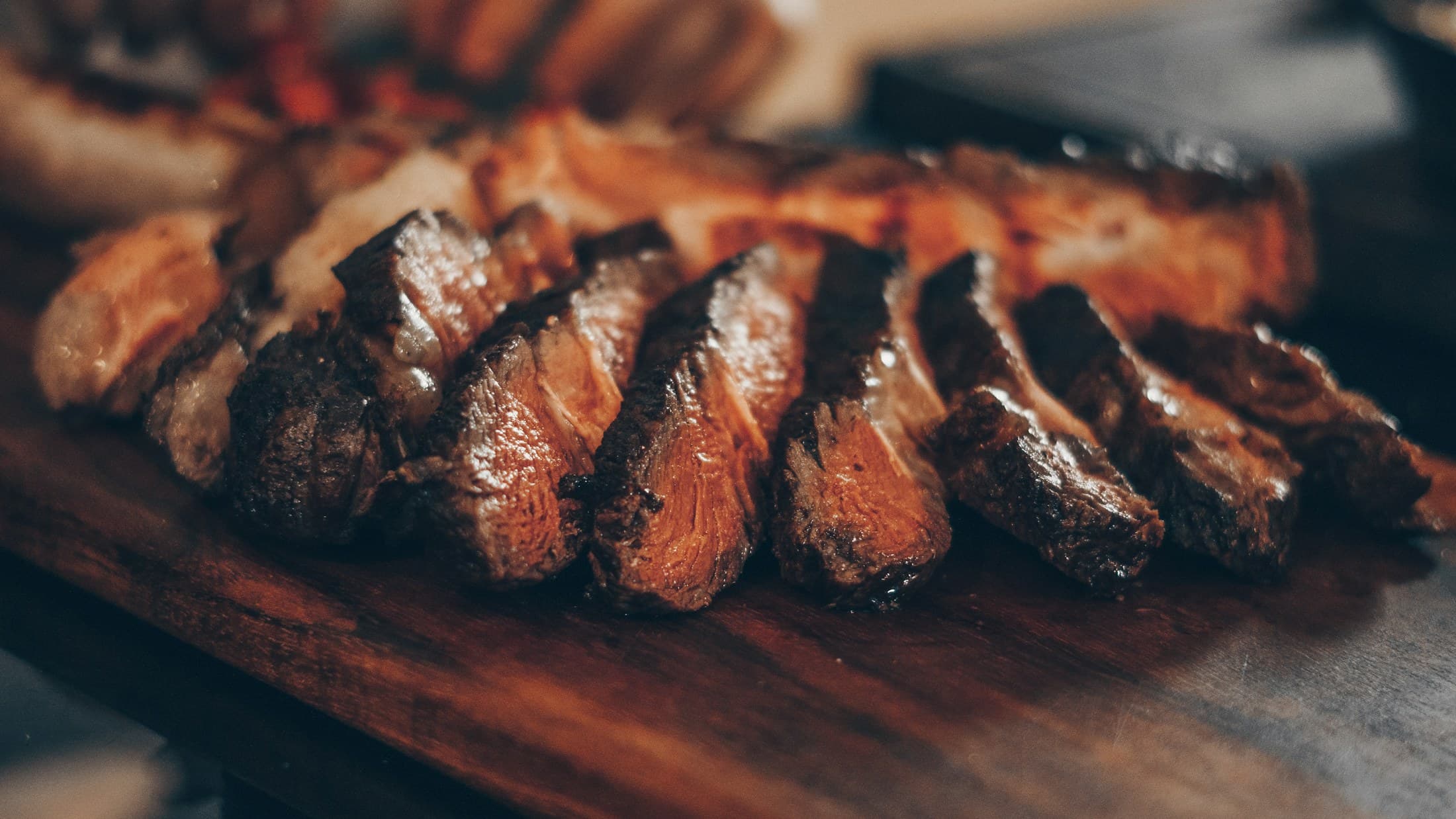 Sliced steak, pink at the centre, on a wooden board.