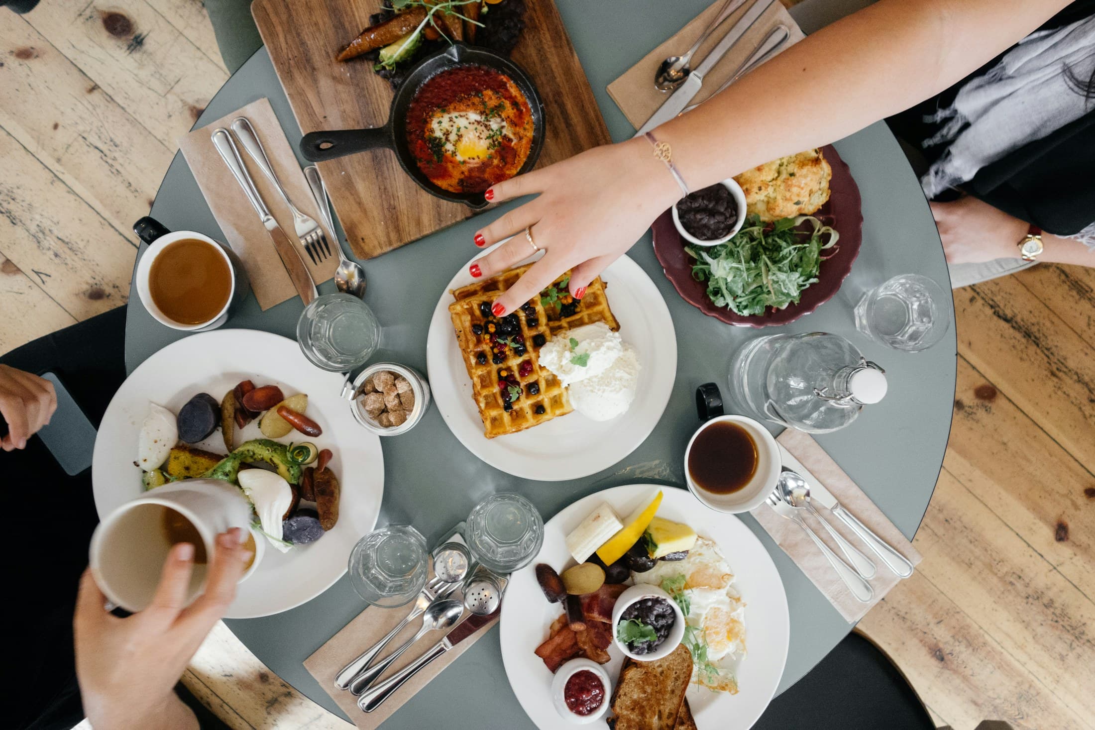 A shared table of small plates seen from above, hands reaching across.