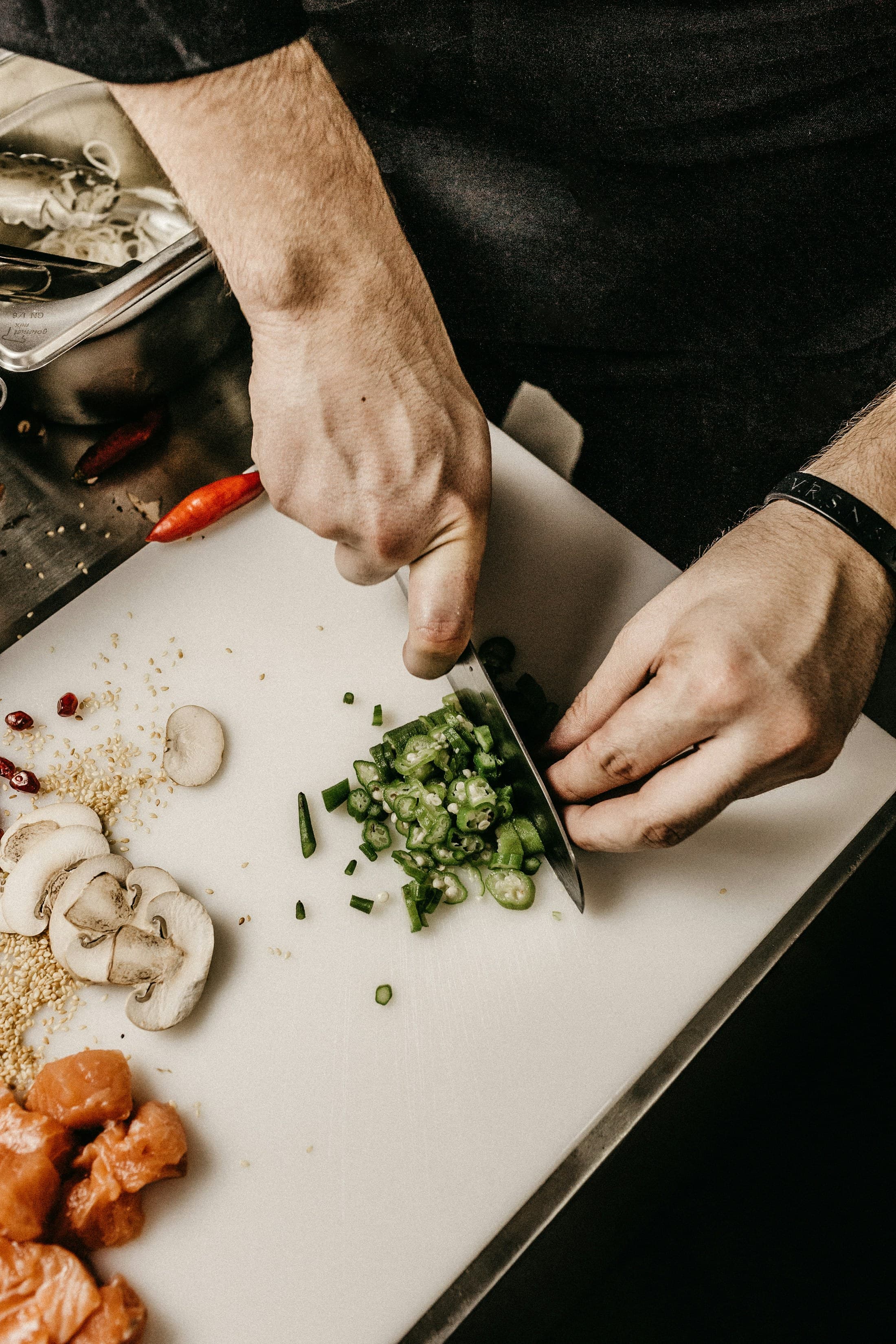 Hands chopping okra and herbs on a white board.
