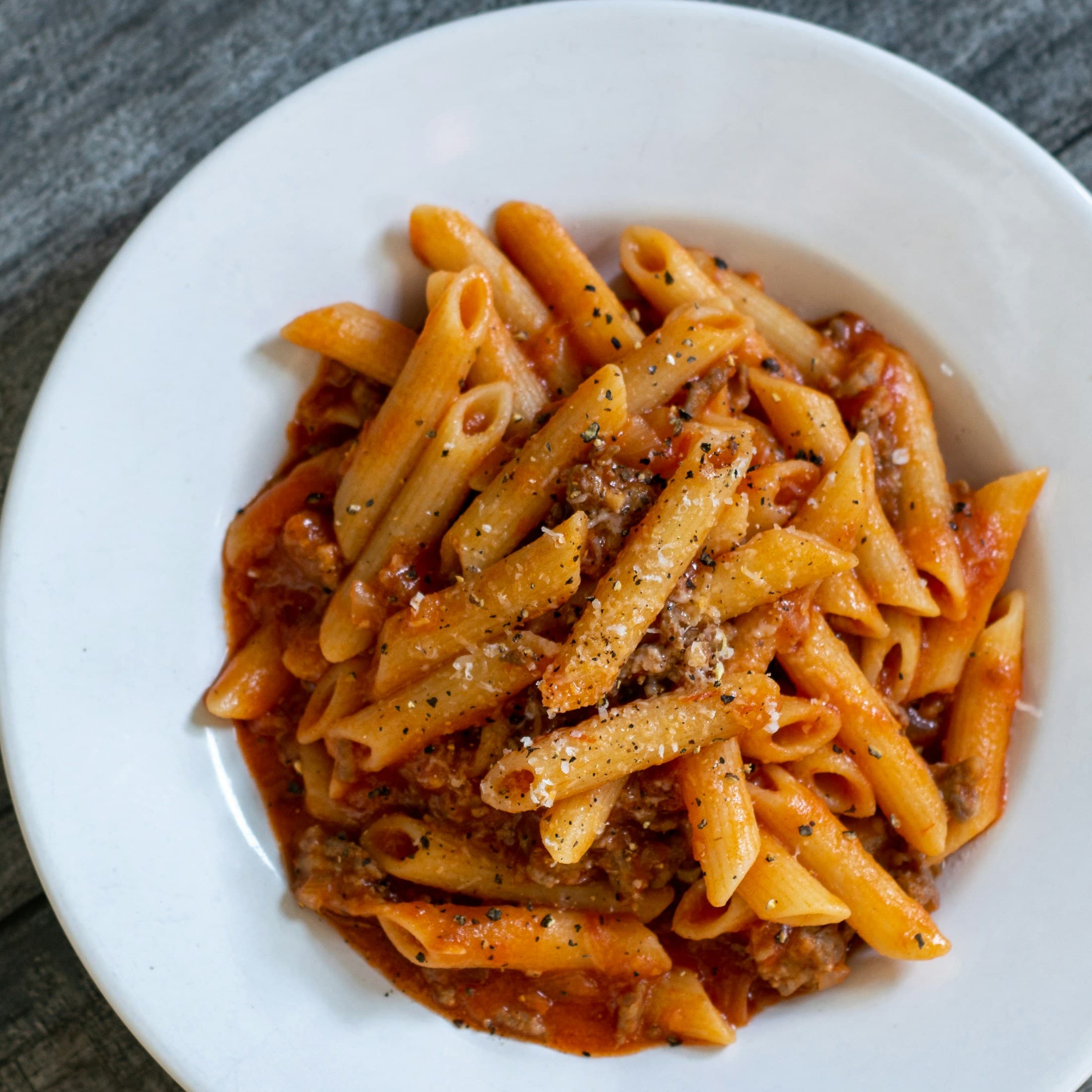 Penne in a slow-cooked meat sauce in a white bowl.