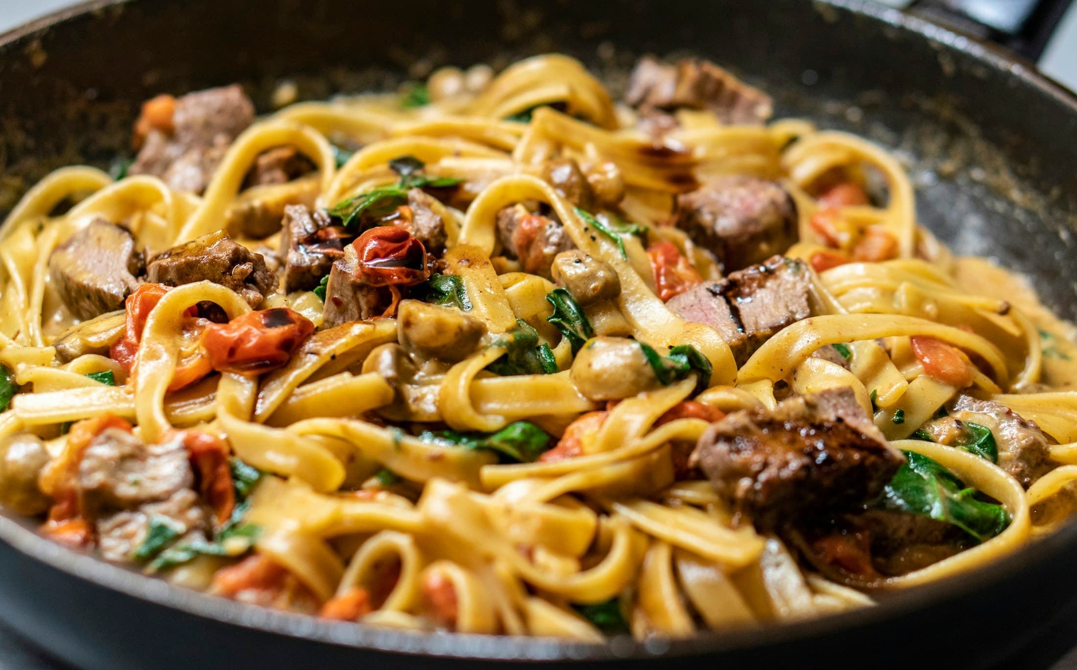 Fresh tagliatelle tossed with beef and mushrooms in a pan.