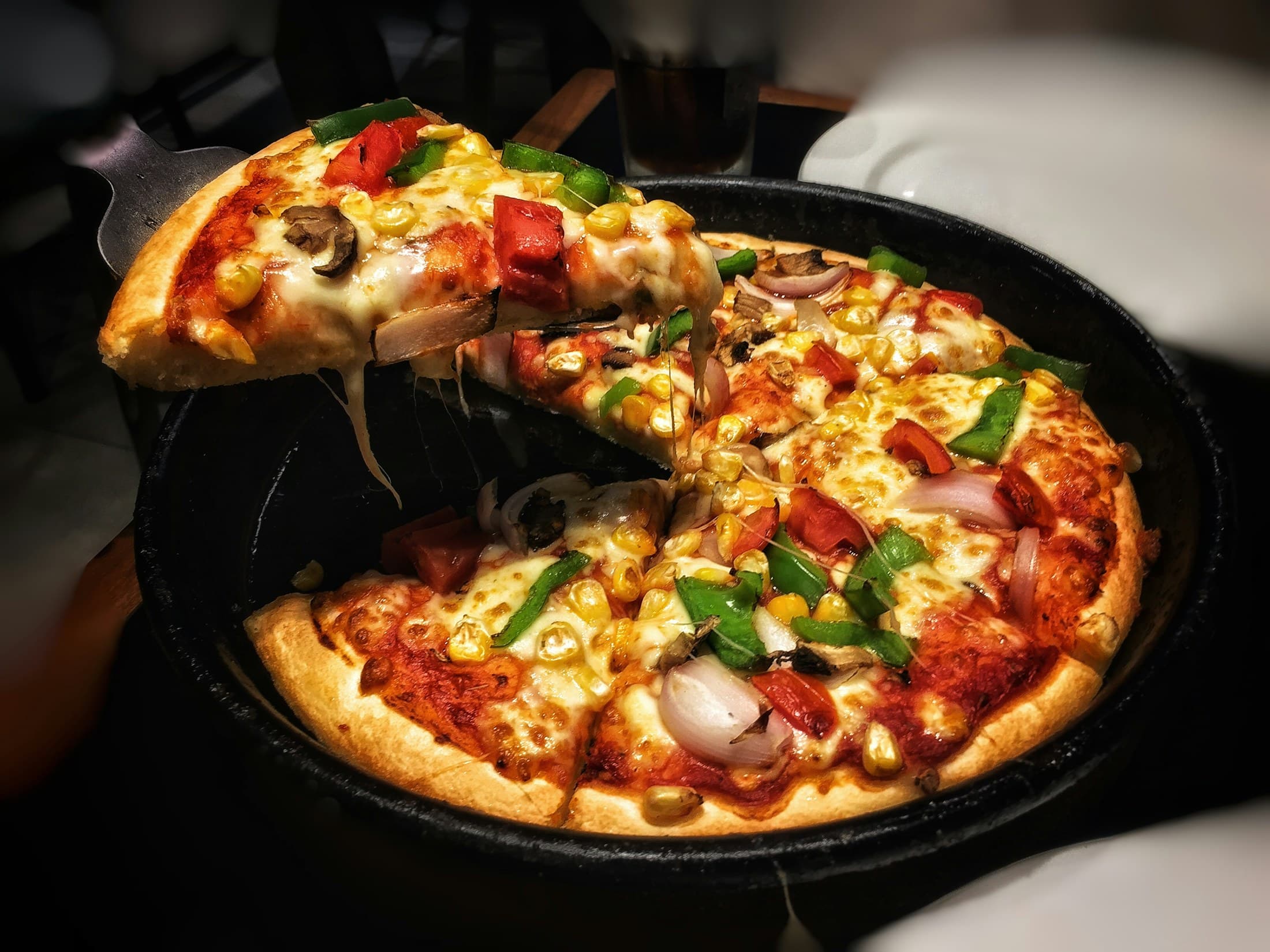 A slice lifted from a pizza baked in a cast-iron pan.